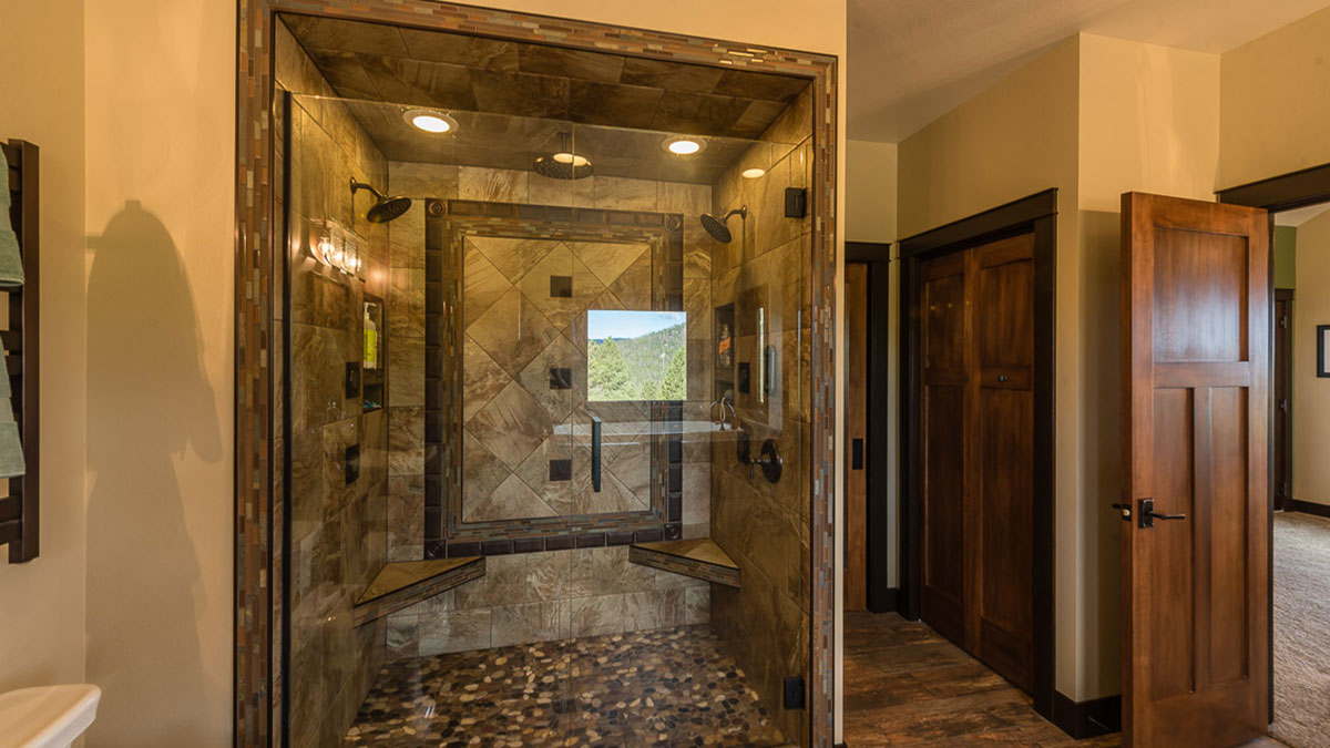 A large walk in shower with glass doors, two seats, a shower head on each side and lined with tile work and a rock floor