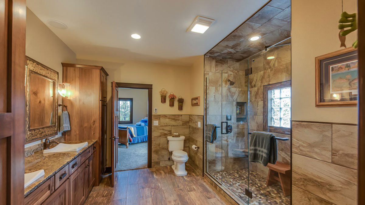 Bathroom with a walk in shower to the right and a granite countertop with custom sinks on the left with a view of the bedroom
