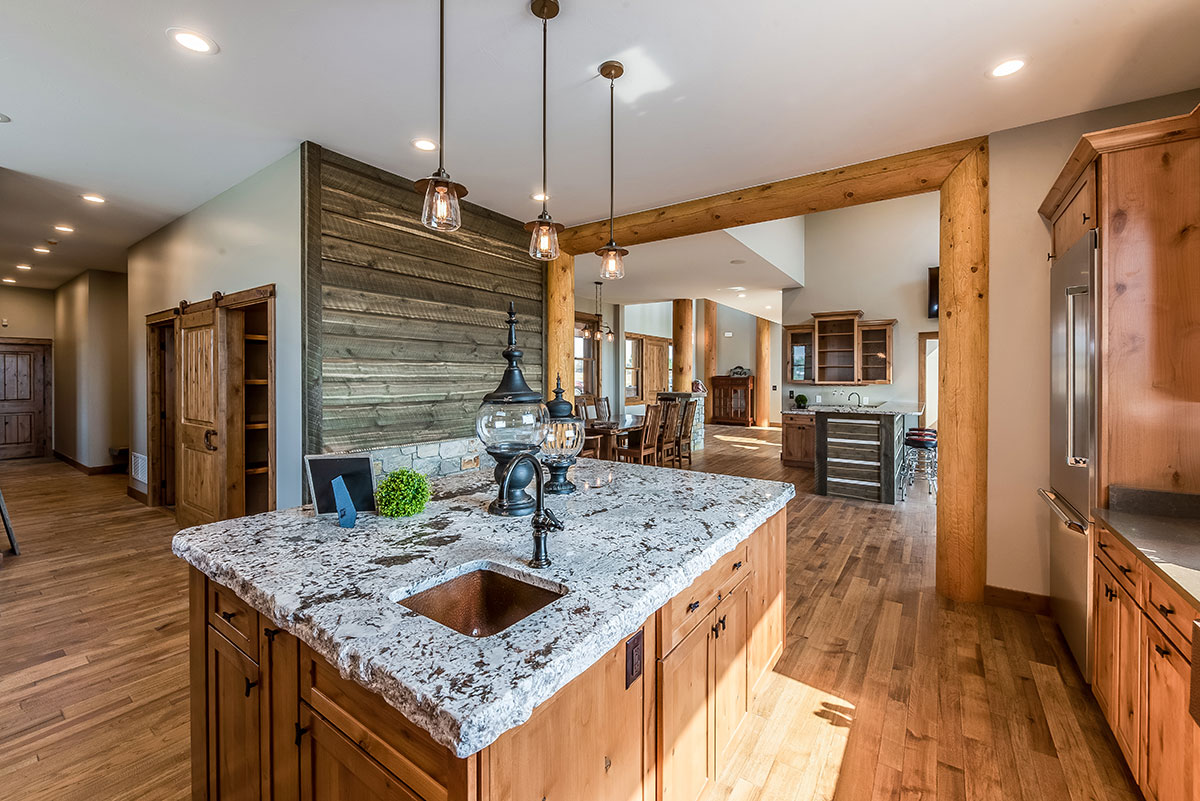 Kitchen island with raw edge granite top, wood floors, a timber frame entrance into the next room with barnwood on the wall