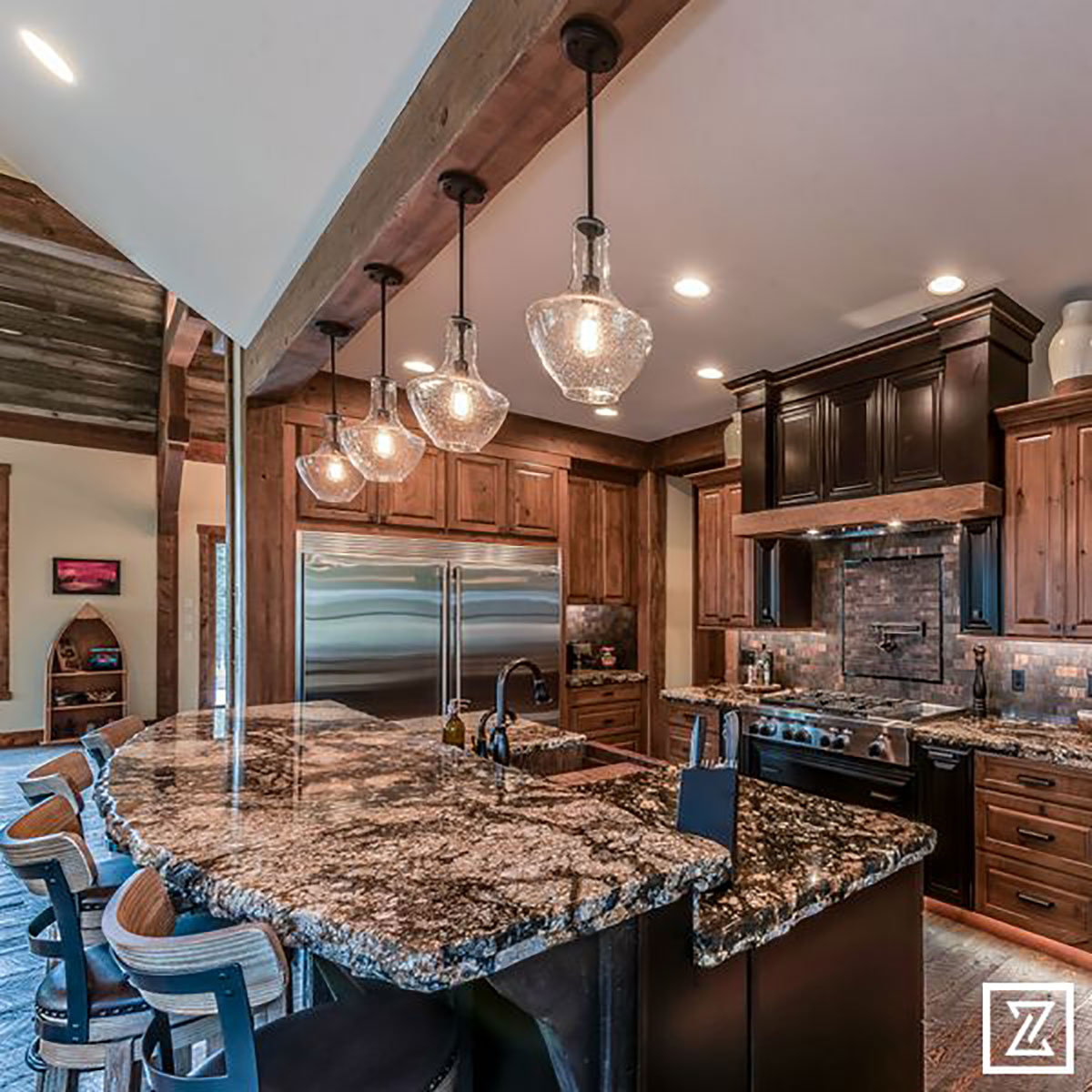 Well lit kitchen with hanging lights over the island with granite countertops and barstools around it