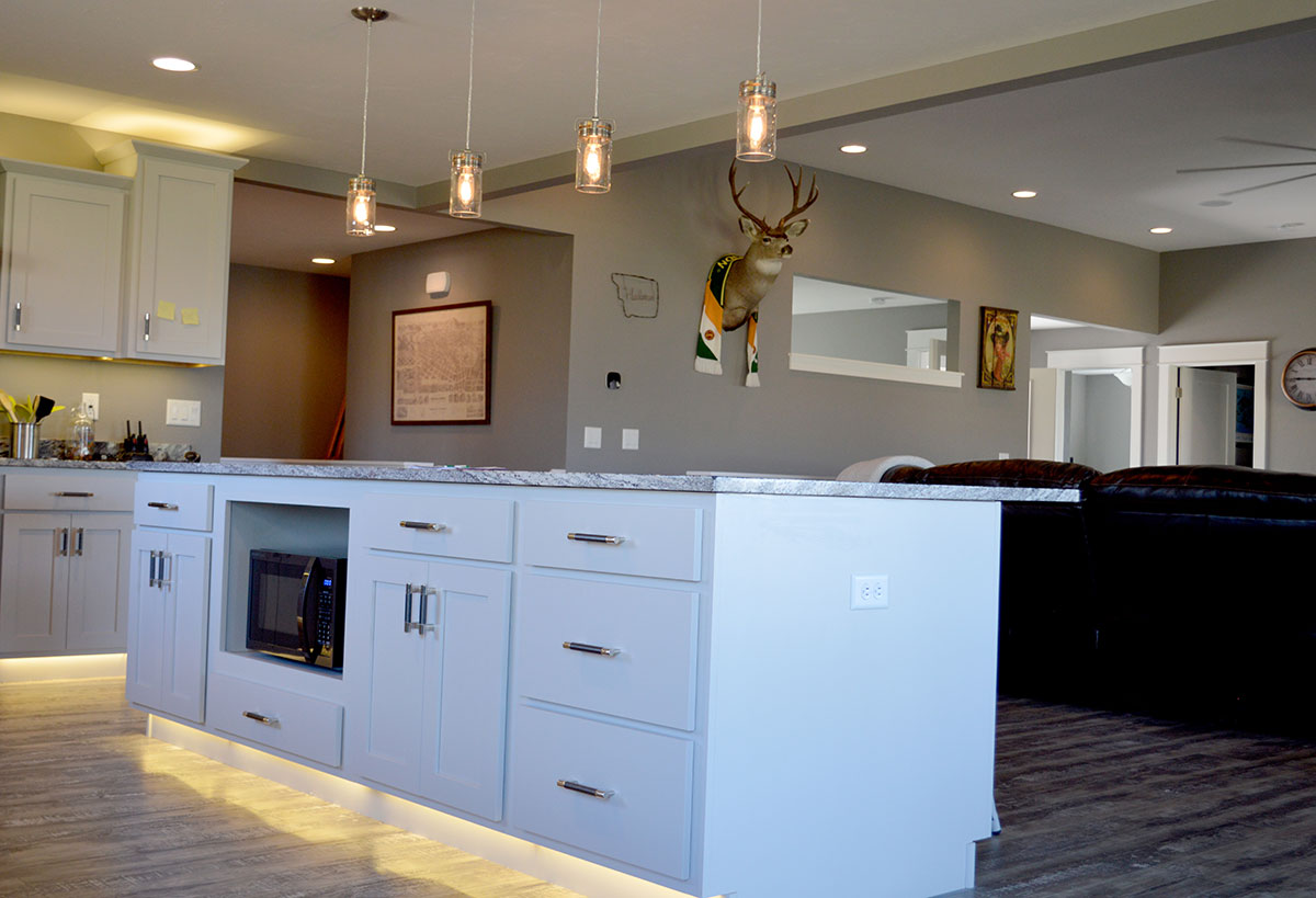 Well lit kitchen with a central island and hanging pendant lights and a view of the living room with a deer mount on the wall